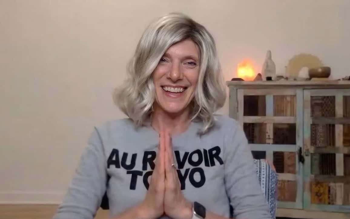 Emilee Garfield smiling with hands in prayer pose in cozy home environment.